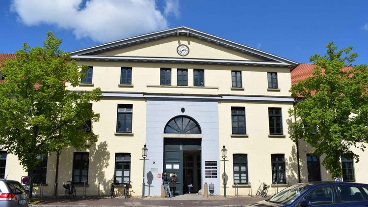 Das Bürgerbüro Mitte in Oldenburg mit heller Fassade, Uhr und Rundbogenfenster.
