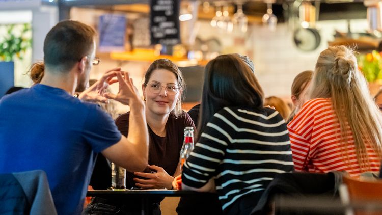 A quiz sitting on a table discussing, with one person holding both hands up shaped like a sphere.