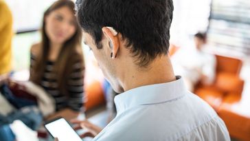 Man from behind, with hearing aid in ear and smartphone in hand