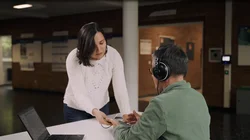 A woman gives a mobile phone to a man wearing headphones to carry out a hearing test