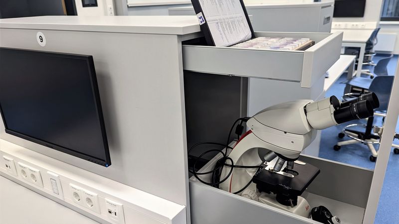 Im Schrank, an dem ein Monitor hängt, verbergen sich zwei Schubladen: Eine große beherbergt ein Mikroskop, eine kleine die Präparate, die damit untersucht werden können.