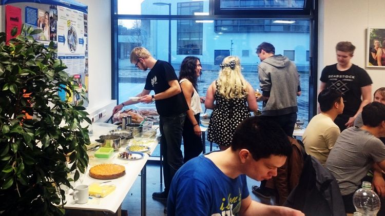 Einige Personen haben sich im IKT für das International Dinner versammelt. Eine Auswahl an Speisen liegt auf dem Tisch.