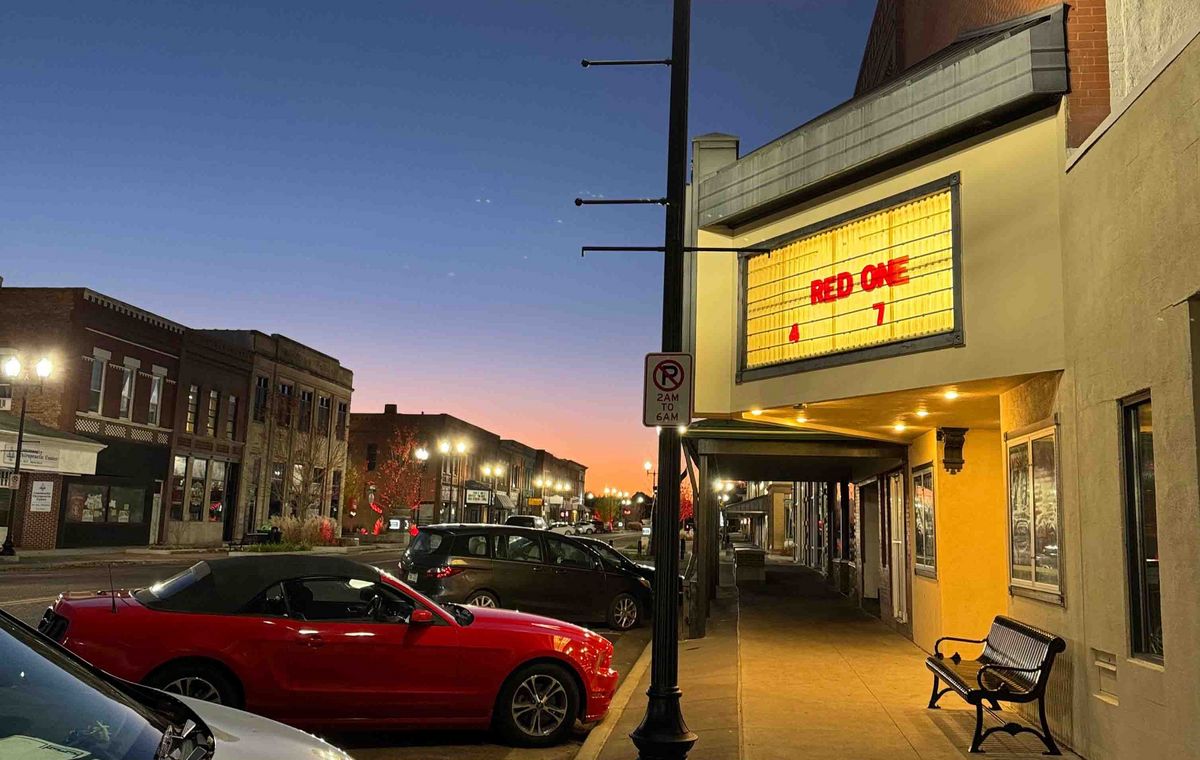 Straßenszene bei Sonnenuntergang mit Kino, Laterne und parkenden Autos.