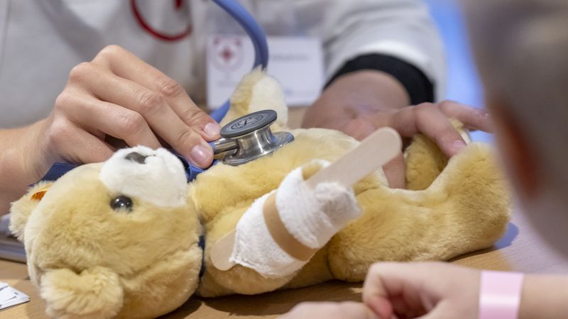 Ein Teddy mit geschientem Arm wird mit einem Stethoskop untersucht. 
