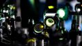 The photo shows an experimental setup. A green laser beam passes through several optical components positioned one behind the other. 