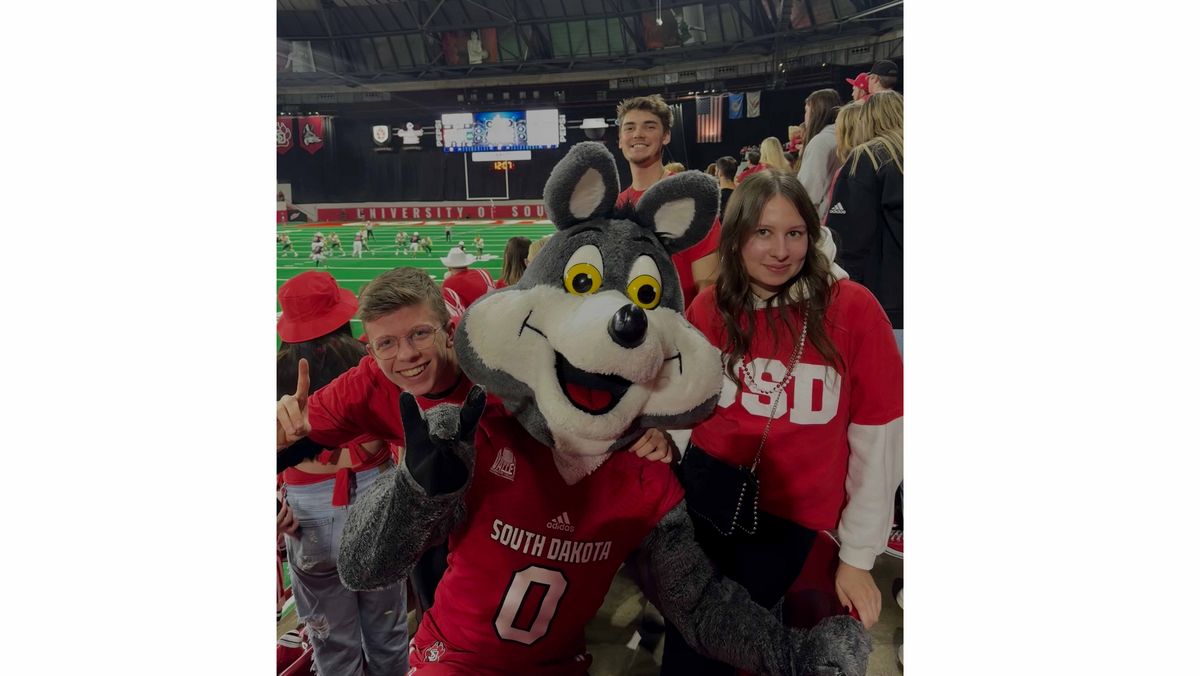 Das Maskottchen der South Dakota Coyotes posiert mit Fans bei einem Footballspiel.