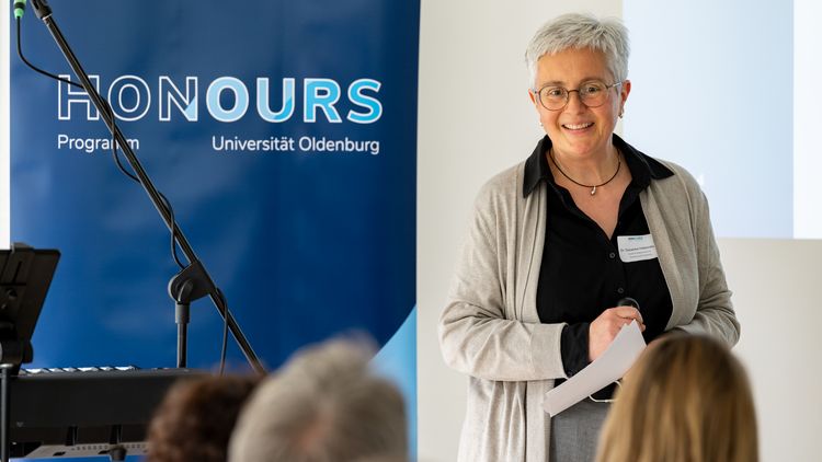 Eine Frau steht vor einem Publikum, daneben der Schriftzug „Honours".