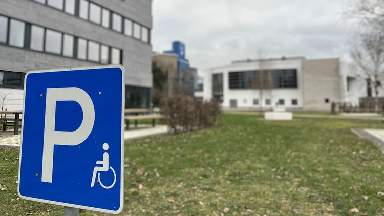In the foreground: sign for a disabled parking space, in the background the lecture hall and the SSC. 