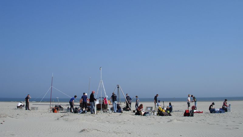 Viele Personen führen Messungen auf einem Sandstrand durch.