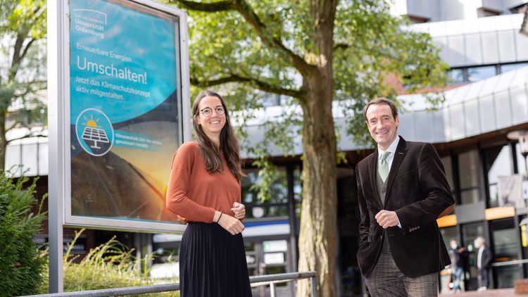 The two protagonists in front of a showcase with a poster highlighting the climate protection project.