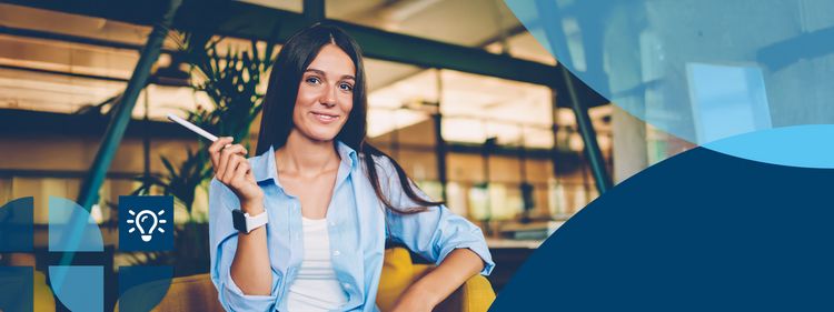 Eine Frau sitzt auf einem Sessel, lächelt in die Kamera und hält einen Stift auf Schulterhöhe hoch.