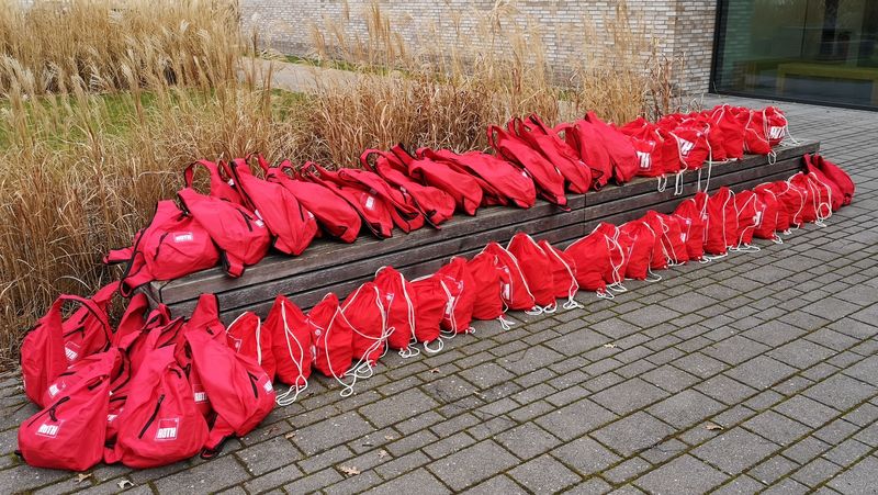 42 rote Rucksäcke liegen auf und vor einer Bank vor dem Experimentierhörsaal in Wechloy.