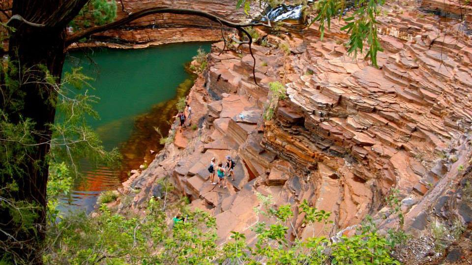 Eine Gruppe wandert an einem felsigen Abhang neben einem türkisfarbenen Wasserloch entlang.