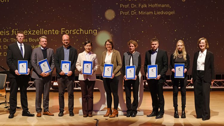The people stand next to each other on the stage with their certificate in their hands.