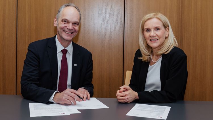 Ralph Bruder und Jutta Günther mit Vertragsunterlagen in einem Besprechungsraum - beide schauen freundlich in die Kamera.