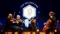 String quartet with two men and women in front of a screen showing ‘The Golden Ear’.