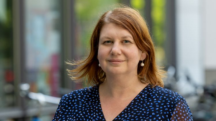 Portrait picture of Yulia Golub. She has half-length dark hair and is wearing a blue top.