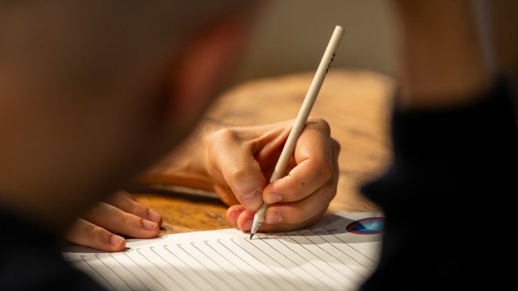 Close-up of a hand holding a pen and filling out a quiz answer sheet.