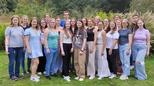 The picture shows the 22 volunteers. They are standing on a lawn, with trees and bushes visible in the background. They are smiling at the camera.