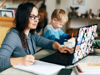 Frau lernt oder arbeitet am Laptop, neben ihr malt ein Kind