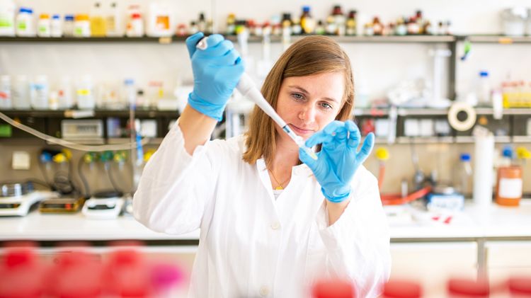 Researcher in the laboratory with pipette, glass bottles in the foreground
